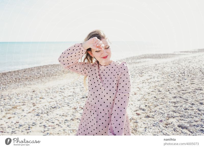 Young woman wearing a pink dress at the beach holidays trendy kawaii casual lifestyle blonde natural beauty attractive pretty fashion model wind windy sea shore