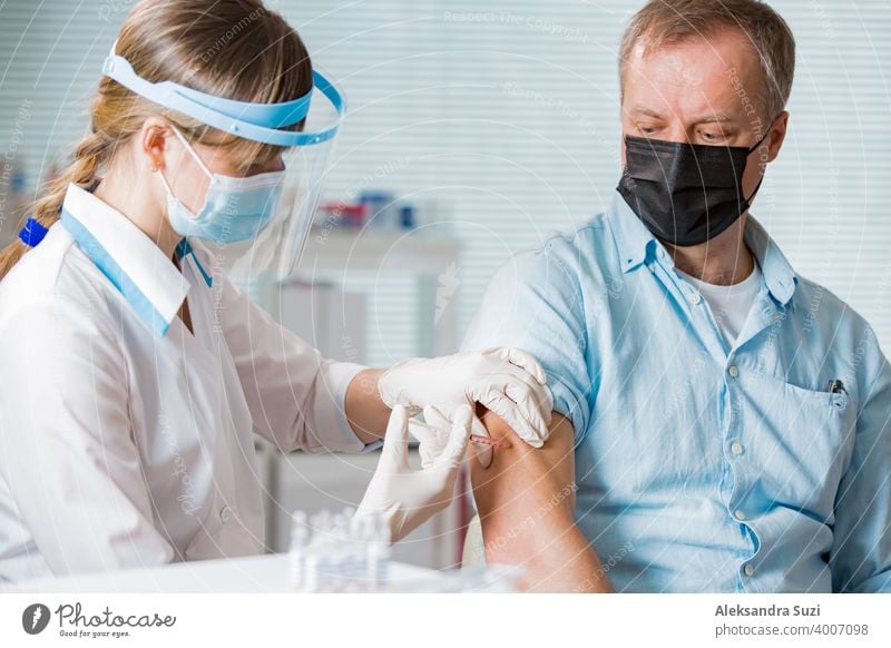 Female doctor with surgical mask and in gloves giving vaccine injection to man in hospital. Vaccination during COVID-19 pandemic arm care clinic coronavirus