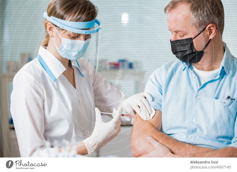 Female doctor with surgical mask and in gloves giving vaccine injection to man in hospital. Vaccination during COVID-19 pandemic arm care clinic coronavirus