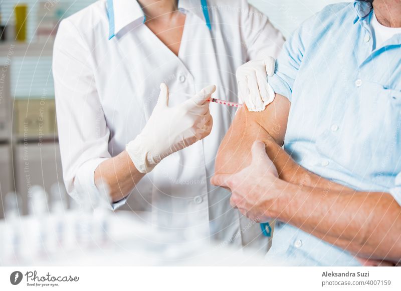 Female doctor with surgical mask and in gloves giving vaccine injection to man in hospital. Vaccination during COVID-19 pandemic arm care clinic coronavirus