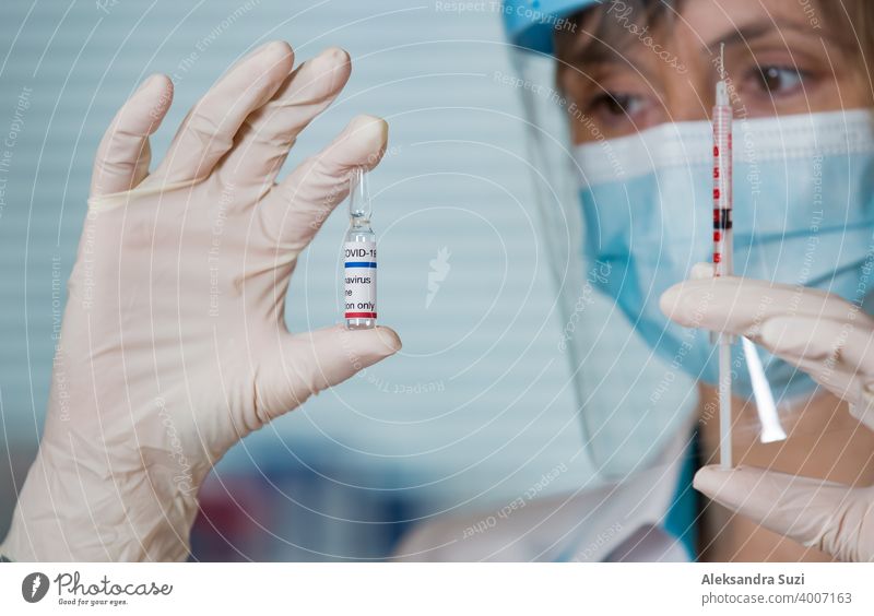 Female doctor with surgical mask and in gloves holding vaccine ampoule and syringe. Vaccination during COVID-19 pandemic arm care clinic coronavirus covid-19