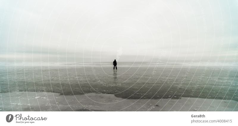 silhouette of a lonely man on ice in the frozen sea background beach climate clouds cloudy coast coastline cold day dirty frost go go away horizon landscape