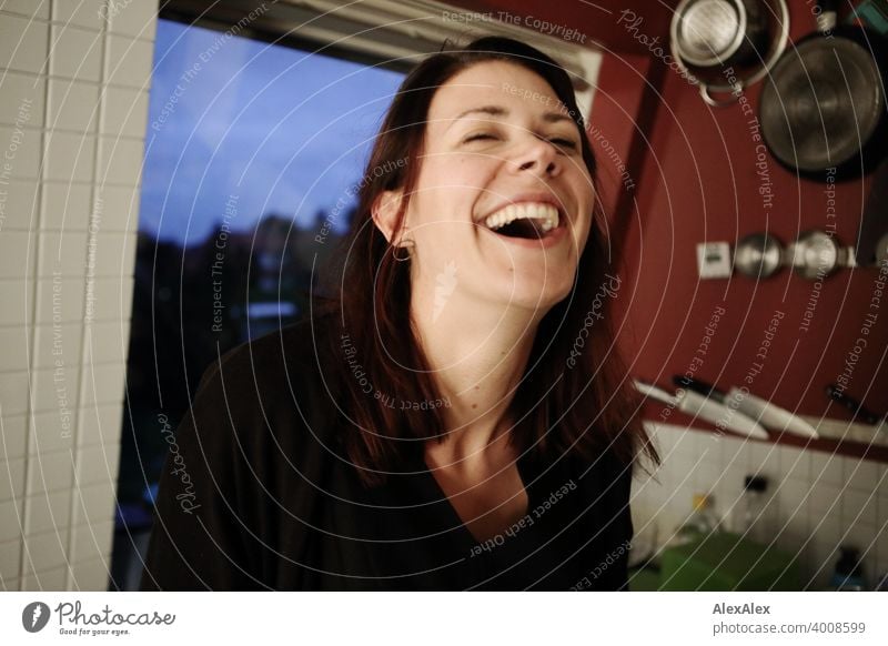 young woman stands in her kitchen and laughs heartily Woman Laughter fortunate Kitchen pretty Large Decompose pots Slim emotionally Face Adults Identity