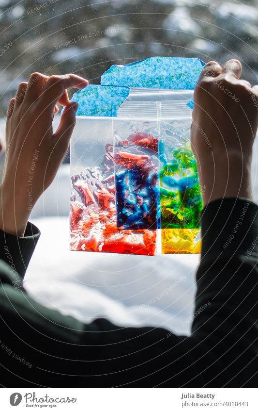 Special needs child holds zip lock baggies of colored gel up to a window to learn about primary colors, color mixing, and sensory play hand touch color theory