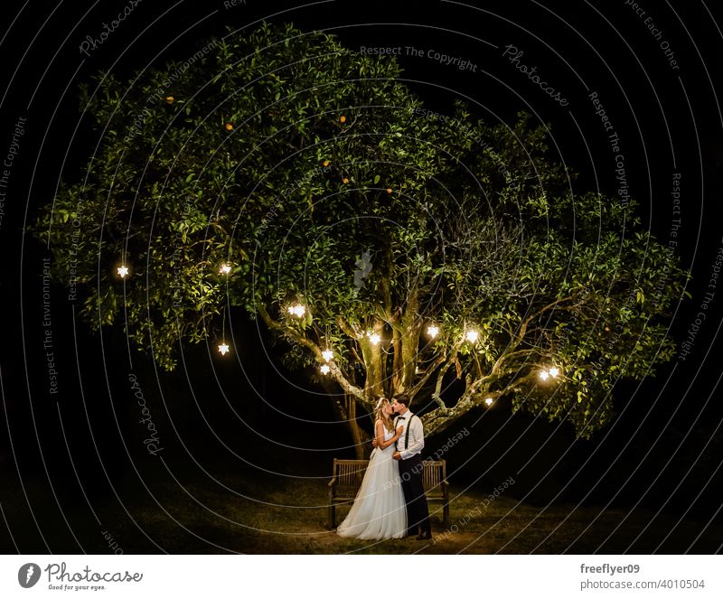 Couple under a tree on their wedding day marriage engagement bride people young attractive copy space night lights pendant nature outside love groom couple