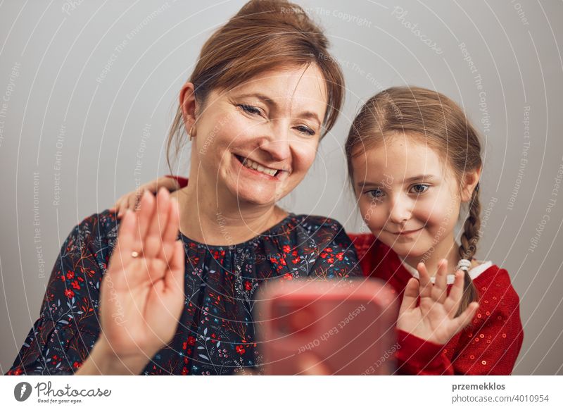 Mother with her little daughter making video call using mobile phone. Woman and little girl talking with relatives. Cheerful family having fun taking selfie photo using smartphone