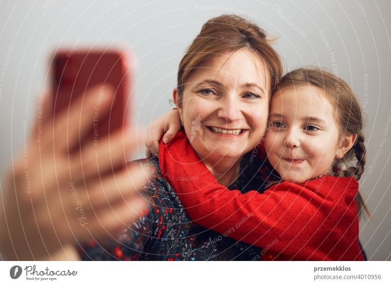 Mother with her little daughter making video call using mobile phone. Woman and little girl talking with relatives. Cheerful family having fun taking selfie photo using smartphone