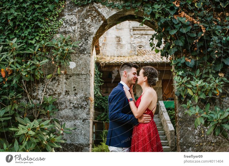 Elegant young couple on a luxurious building with vegetation elegant prom kiss 20s dress suit red first time event caucasian luxury castle ancient tuxedo