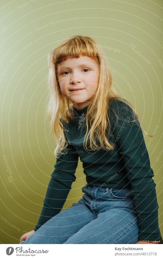 portrait of cute blonde girl against green background bangs blond hair casual clothing child childhood colored background emotion hairstyle indoors innocence