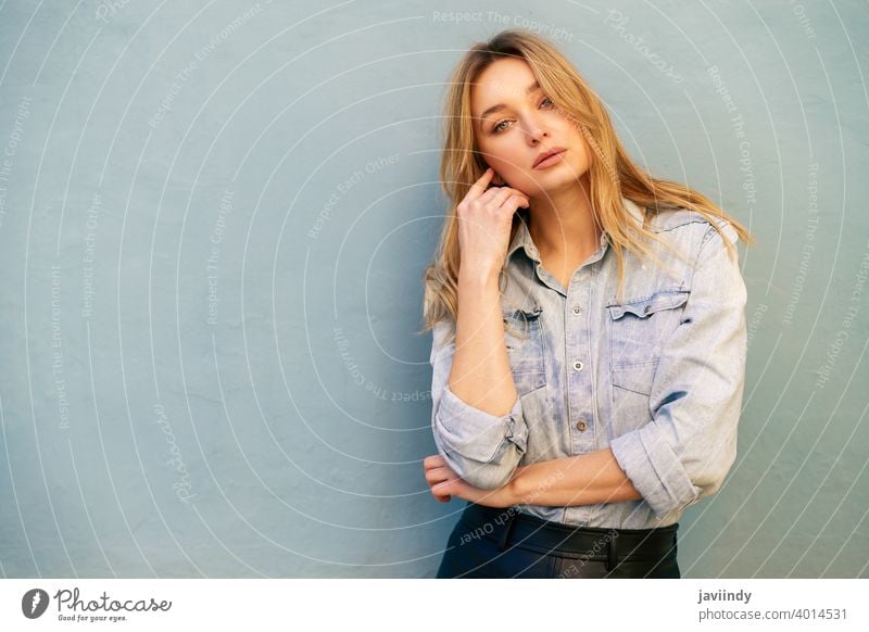 Blonde woman wearing denim shirt and black leather skirt standing in the street. girl female blonde russian blue eyes portrait fashion outdoors lady hairstyle