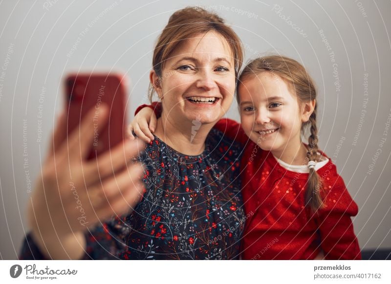 Mother with her little daughter making video call using mobile phone. Woman and little girl talking with relatives. Cheerful family having fun taking selfie photo using smartphone