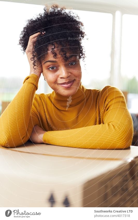 Portrait Of Confident Young Woman Resting On Removal Box As She Moves Into Her New Home woman house buying unpacking boxes home new home first home portrait