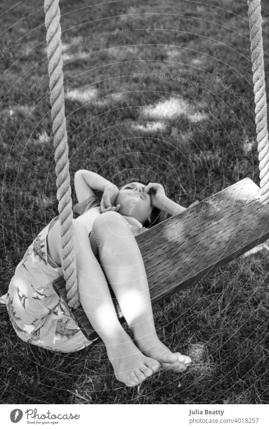 Boy with Autism laying on ground with legs draped over swing; playing in his own unique way on a warm summer day special needs autism boy child preteen rope