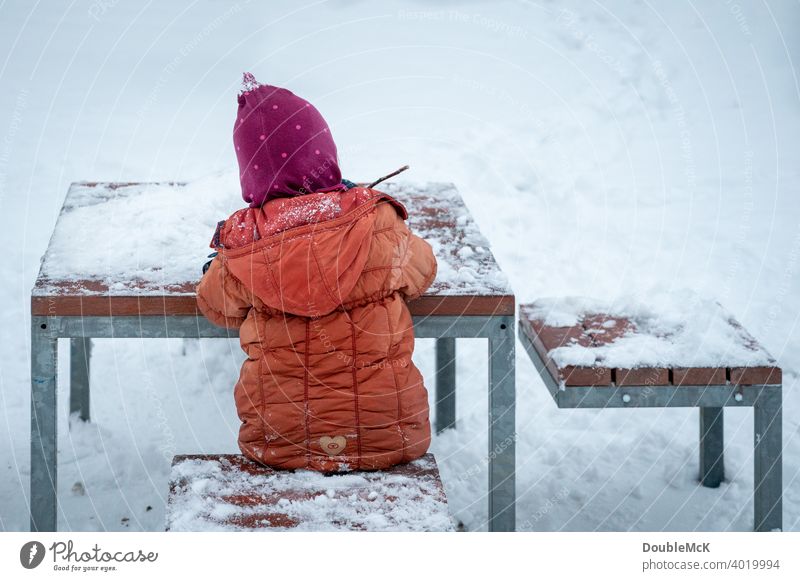 A child sits outside at the snowy table in the snow and plays Day Exterior shot naturally Life Joy Cold cold season Snow look away Winter chill 1 snow-covered