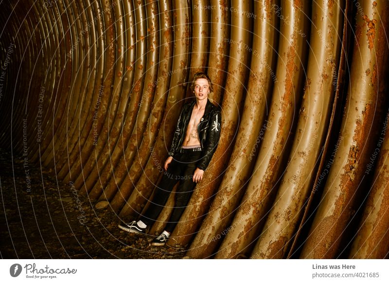 Wild boys from the band like our model right here always look like rockstars. Inked and dressed in a black leather jacket. Looking straight into the camera in this underground with rusty metal all around.