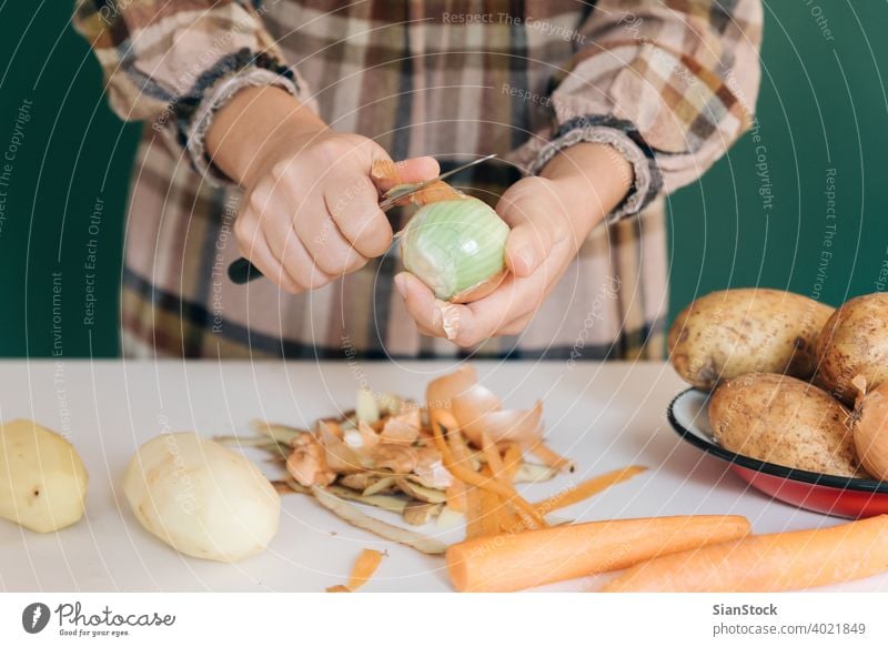 Woman peels off onions at her kitchen on white marble, to prepare her food. woman vegetable potatoes vegan home peel-off peeling carrots organic green cutting