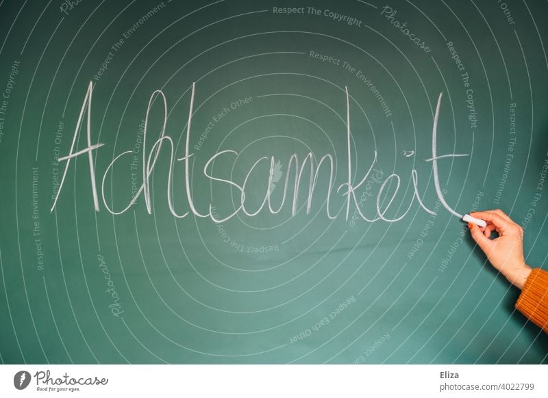 Hand writes the word mindfulness on a blackboard attentiveness Write Word well-being Meditation relaxation Buddhism Consciousness Happy stress reduction