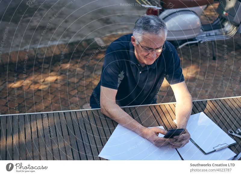 Small business owner working on mobile phone with workshop in background caucasian male man 60's hobby hobbyists candid authentic people home hobbies craft