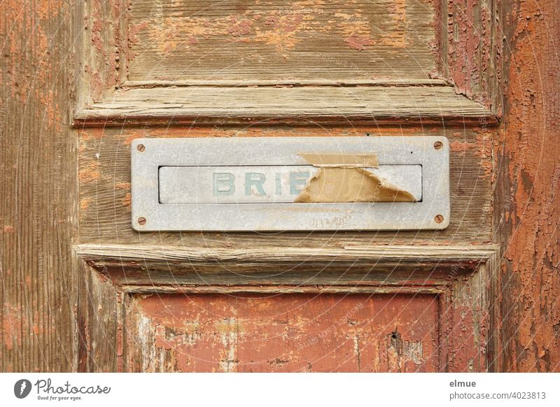 old, pasted mailbox slot with a flap that says "LETTERS", made of metal in an old wooden door, where the brown paint is peeling off / write letter / e-mail / mailbox company