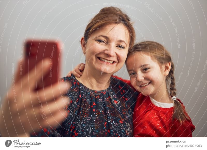 Mother with her little daughter making video call using mobile phone. Woman and little girl talking with relatives. Cheerful family having fun taking selfie photo using smartphone