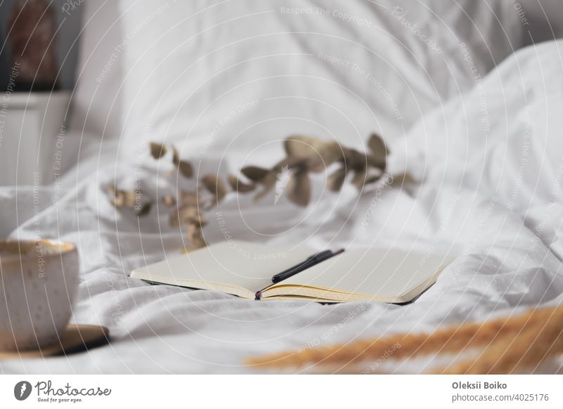 Open notepad with blank pages in textile white background, dried flowers and cup of tea. Tranquil and mindful home living, staying in bed, hand writing in a note book concept