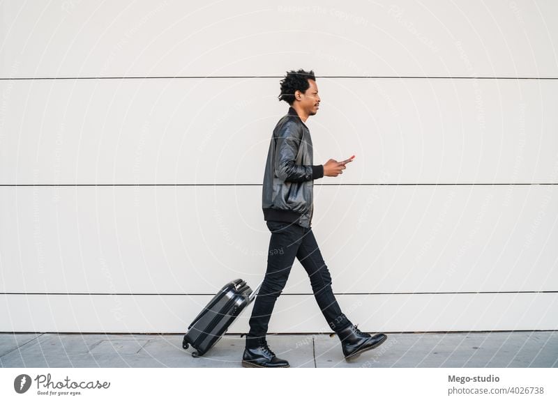 Tourist man using his mobile phone and carrying suitcase outdoors. tourist communication business text black cell sms holiday city journey enjoy telephone afro