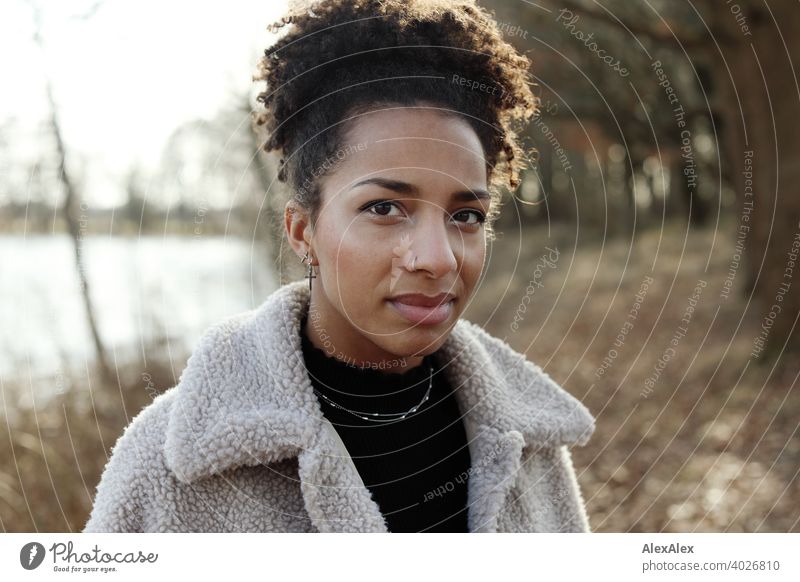 Young woman in fur jacket standing in nature by a lake Woman Athletic Dark-haired Long-haired pretty Strong daintily naturally Curly Slim Back-light Nature out