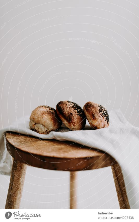 Three sourdough bun with poppy seed and sesame on a napkin on a wooden stool breakfast bread gluten bread roll pastry bakery fresh morning flour whole meal food