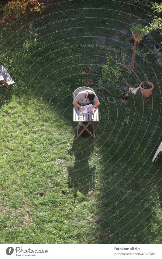 Bird's eye view of a young man sitting at a small table in the garden and writing in a notebook. Young man Garden table Study study Write Workplace