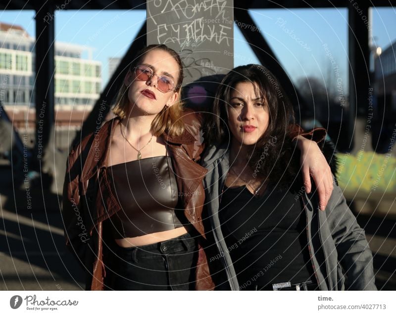 Lara and Estila Woman Long-haired Stand Earnest Cool Friendship Coat Easygoing Blonde Dark-haired Architecture Bridge sunny Sunlight togetherness