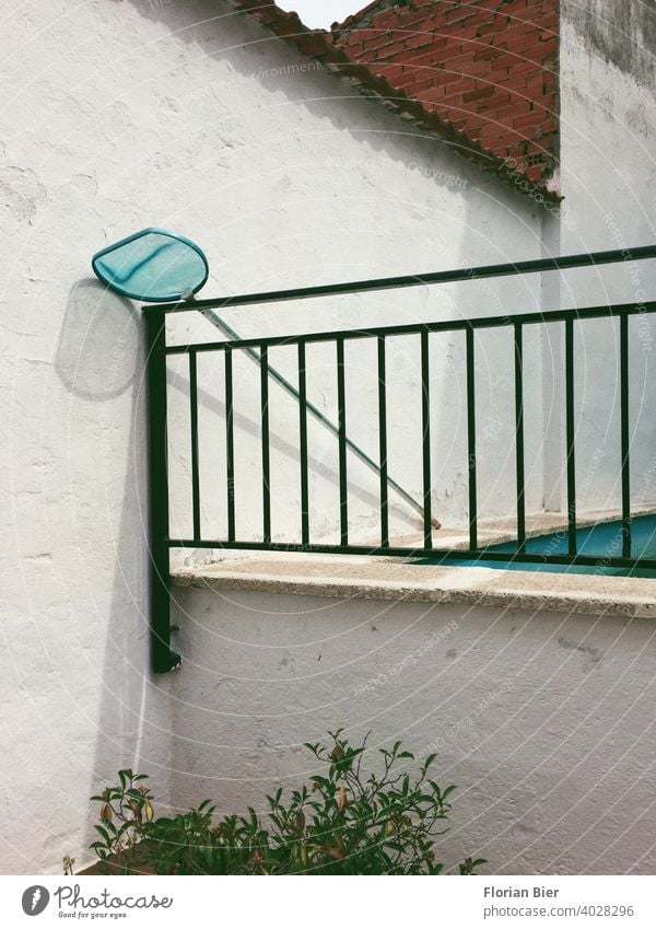 Pool landing net leaning against an iron railing next to a swimming pool in the backyard Landing net Backyard Swimming pool Wall (barrier) brick Wall (building)