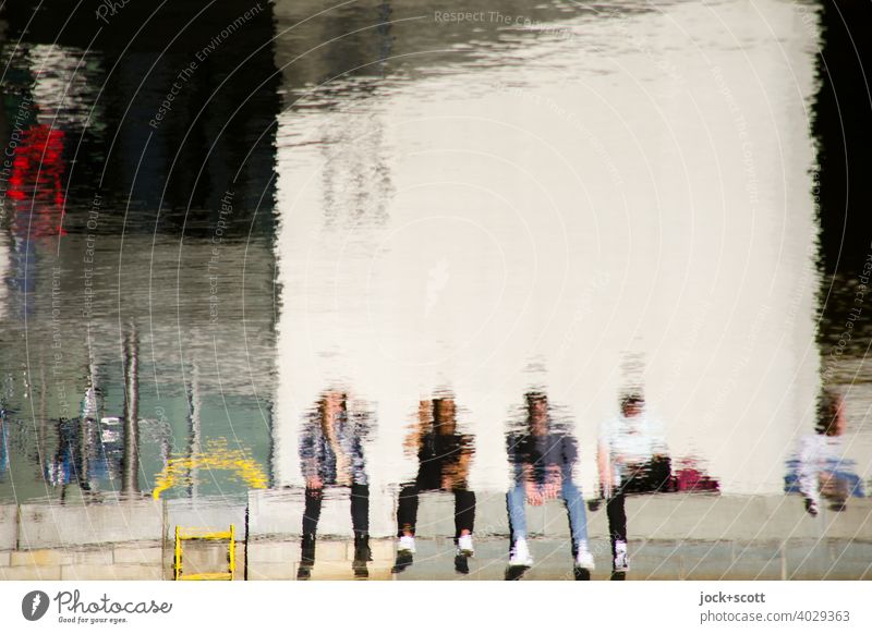 Four people sitting in the sun by the quiet river Modern architecture Spree Surface of water Reflection hazy Spreebogen sunshine parliament building blurriness