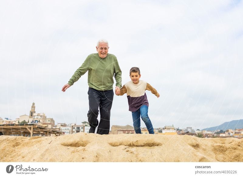 Little boy and his grandfather running on the beach active adult caucasian child childhood children elderly enjoying family generations grandchild grandchildren