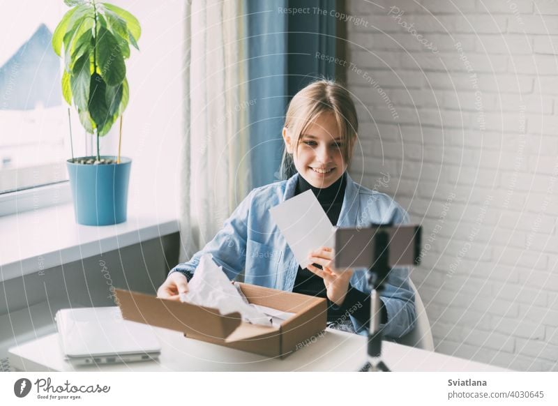 A teen blogger records a video and unpacks a package for his blog on a smartphone on a tripod at home. Communication of a video blogger girl on social networks with subscribers and friends.