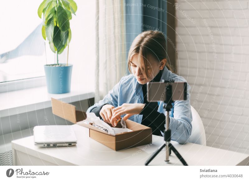 A teen blogger records a video and unpacks a package for his blog on a smartphone on a tripod at home. Communication of a video blogger girl on social networks with subscribers and friends.