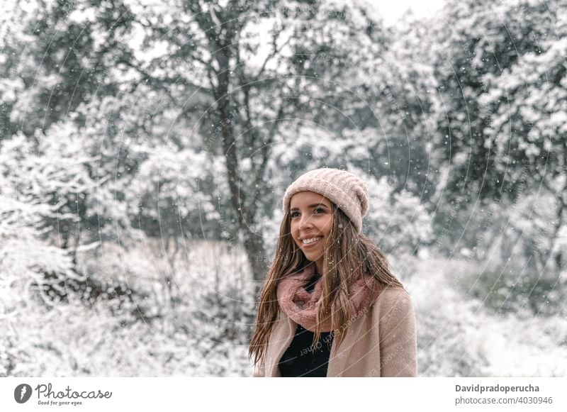 Woman in outerwear walking in snowy woods winter forest carefree enjoy wintertime snowfall stroll smile content warm clothes weekend cheerful happy touch plant