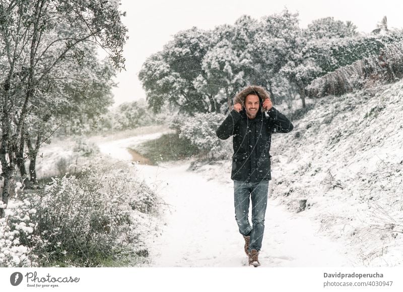 Smiling man in outerwear walking in woods in winter forest smile stroll snow snowfall enjoy cheerful cold season warm clothes jacket path nature happy