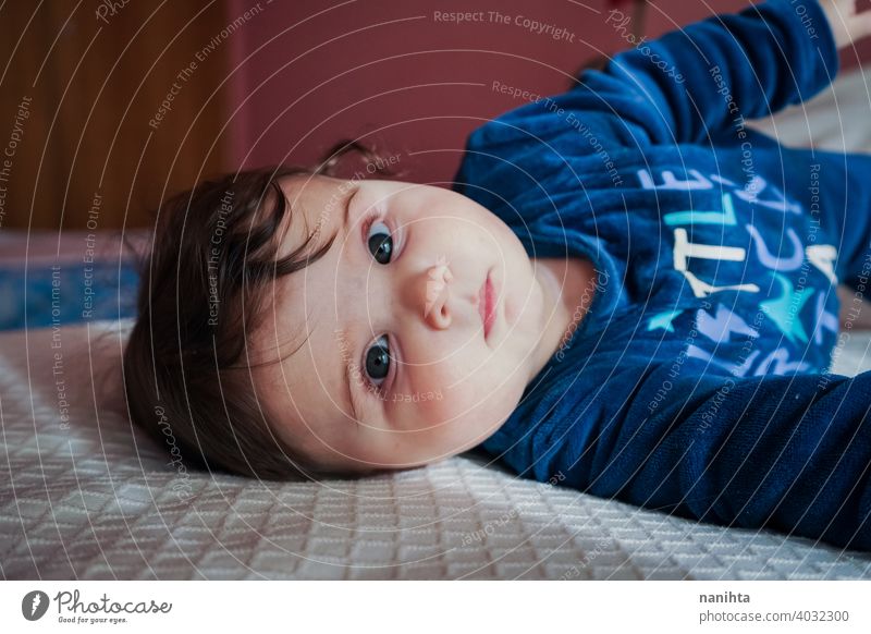 Little baby in blue lying down on a bed babyhood cute lovely girl bedroom home family adorable pajama playful face pretty brown hair blue eyes comfort lazy cozy