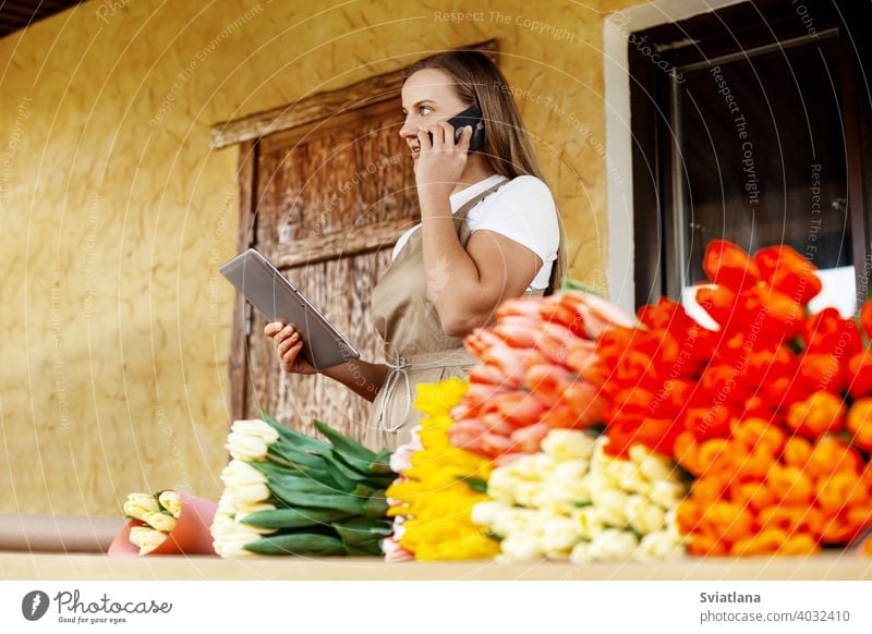 A young female florist with a tablet in her hands is talking on the phone and making an order for her store. Small business. Valentine's Day and Women's Day.