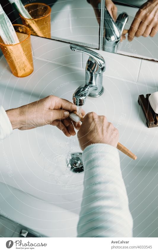 Old woman washes bamboo toothbrush with water and washes her teeth health care mouth bathroom female white age dental elderly mature senior person smile aged