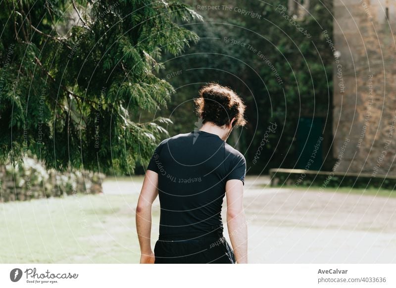 A close up of a long hair male running between the trees during a sunny day in the park 20s exercising horizontal marathon runner sprinting touching jogging