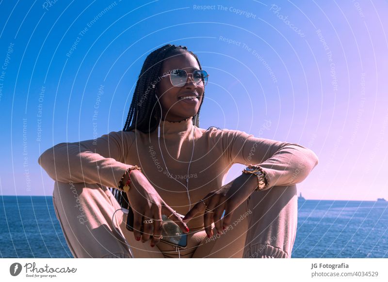 Closeup portrait of young black afro girl smiling with headphones and blue sky background, pretty afro girl transmitting positivity and peace. positive music