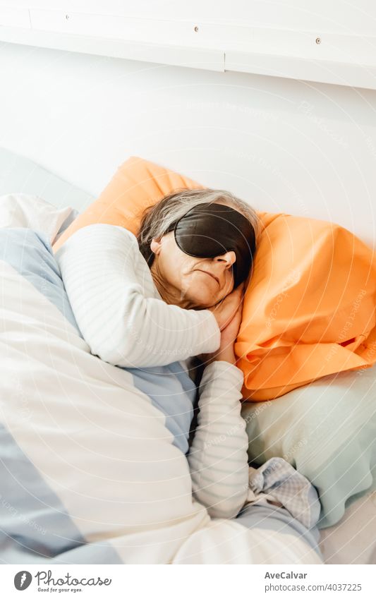 An old lady sleeping using a face mask in a modern bedroom woman senior night grey-haired morning pajama grandmother expression rest pink portrait beautiful