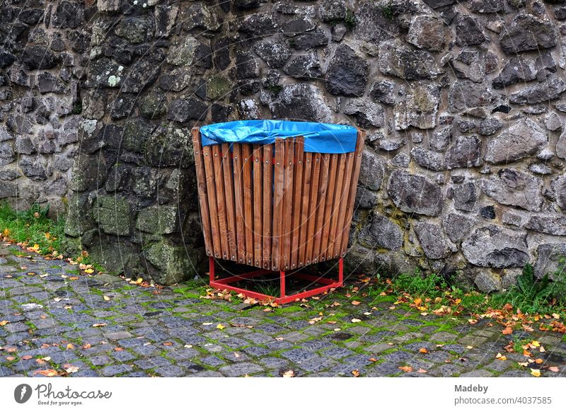 Rubbish bin made of brown wood with blue plastic bag in front of old brickwork in the courtyard of Gleiberg Castle in Wettenberg Krofdorf-Gleiberg near Giessen in Hesse, Germany