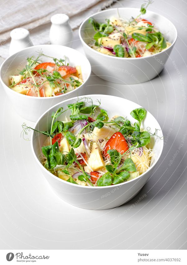 Fruit salad with strawberries, pineapple pieces, herbs, red onions and cheese in white ceramic bowls on a light background. Ideas and recipes for a healthy diet. Vegeterian food. Vertical shot