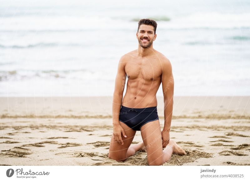 Handsome man on his knees on the sand of the beach sexy male muscular handsome healthy water people fit sea model abs vacation fitness chest strong attractive