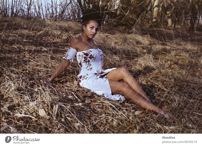 Young woman sitting in nature and looking skeptically into the camera - analog portrait Woman Athletic Dark-haired Long-haired pretty Strong Graceful naturally