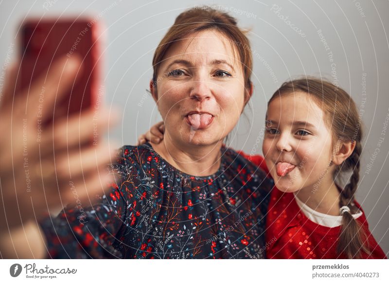 Mother with her little daughter making video call using mobile phone. Woman and little girl talking with relatives. Cheerful family having fun taking selfie photo using smartphone