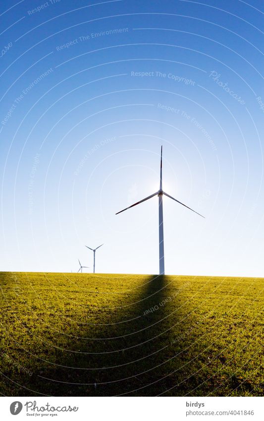 Wind turbines on the field backlit against blue sky. Shadow cast by mast, sun behind generator Wind energy plant regenerative energy Renewable energy