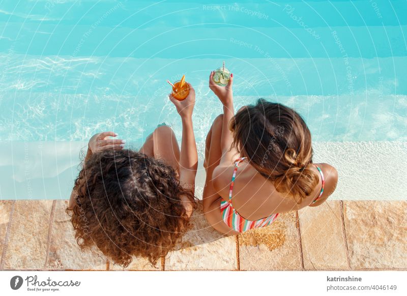 Two young women in swimsuits relaxing and drinking tropical cocktails mojito pool water Summer friends party multiethnic Together caucasian spanish Young